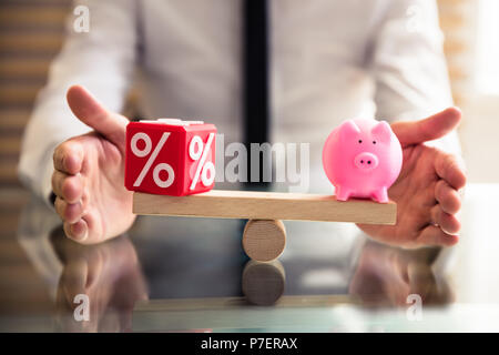 Die schützende Hand Balance zwischen Rot Prozentsatz kubische Block und Sparschwein auf hölzernen Wippe Stockfoto