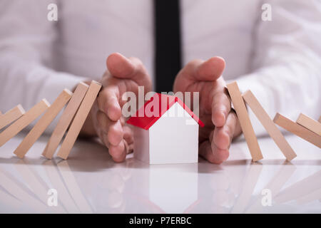 Nahaufnahme der Kaufmann schützende Hand Haus Modell von sinkenden Holzklötze auf weißem Schreibtisch Stockfoto