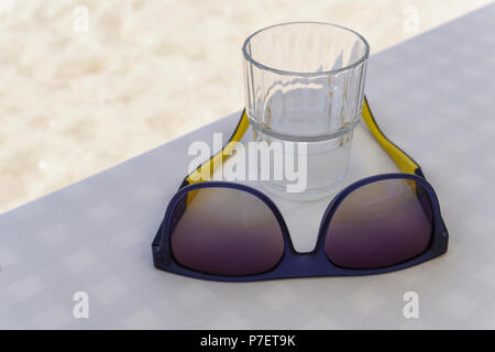 Sonnenbrille auf Tisch im Restaurant mit alkoholischen Getränken. Glas Ouzo auf die Felsen am griechischen Taverne mit weißer Bettwäsche Tischdecke. Stockfoto