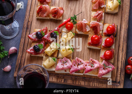 Vorspeisen Tabelle mit italienischen Antipasti, Snacks und Wein in Gläsern. Brushetta oder authentische traditionelle spanische Tapas, Käse Vielfalt Brett über grauer Beton Hintergrund. Ansicht von oben, flach Stockfoto