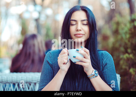 Die Liebe zum Kaffee. Portrait von süße Mädchen trinken Ihren Kaffee auf dem Balkon und über Terrasse mit Green Bush Hintergrund, tragen Blau Grau. blo Stockfoto