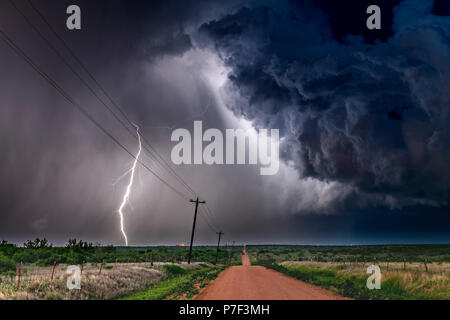 Eine nächtliche, tornadic mezocyclone Gewitter schießt Schraube von Strom auf den Boden und leuchtet das Feld und Schmutz der Straße im Tornado Alley. Stockfoto