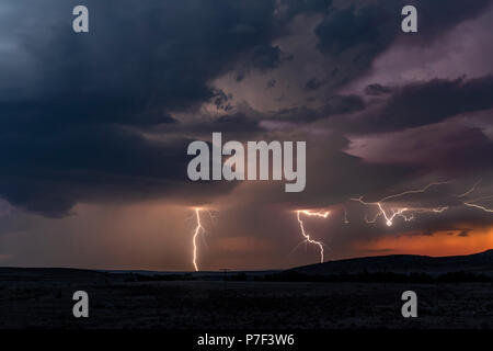Eine große Blitzschlag in der Dämmerung in einer offenen Ebene gegen einen tiefen, dunklen orange Sonnenuntergang und stürmischen Himmel umrahmt. Stockfoto