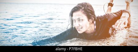 Junge Frau über Surfbrett im Wasser schwimmen Stockfoto