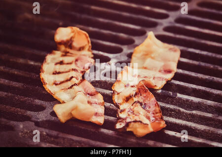 Zangen Holding knusprige geräucherte gegrillte Grill Speck Scheibe, auf bbq Rauch Grill zubereitet, aus der Nähe. Streifen auf die speckscheiben. Die Zutaten für die Sa Stockfoto