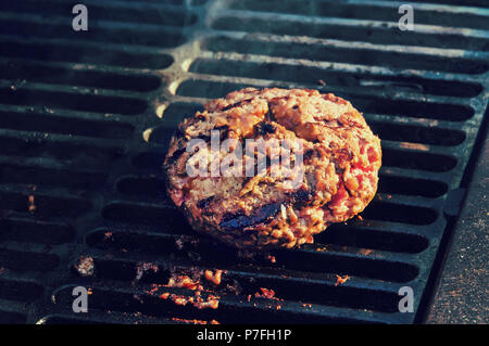 Kochen Burger auf heißen Grill mit Flammen. Grossen dicken Patty Rinderhackfleisch mit gebratene Kanten auf den Grill. Lecker Patty Stockfoto