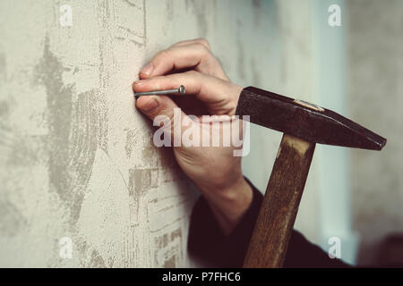 Nahaufnahme der Handwerker hämmern einen Nagel an Bord. Konzept der Reparatur und Renovierung. Guy hämmern einen Nagel in eine Wand aus Gips. Stockfoto