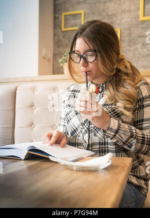Hübsches Mädchen trinken Erdbeere bananne Smoothie und Ihr interessantes Buch lesen im Cafe Stockfoto