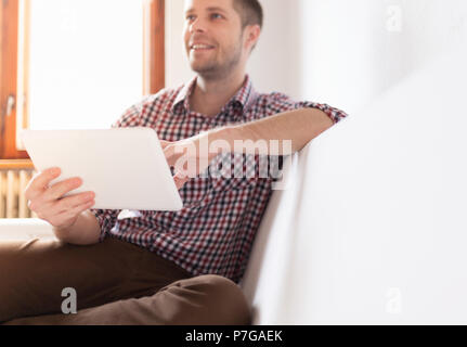 Schöner Mann auf dem Sofa zu Hause sitzen, mit einem digitalen Tablet Stockfoto