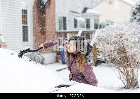 Junge Frau Reinigung Auto Windschutzscheibe von Schnee, Eis mit Pinsel und Schaber Werkzeug bei Schneefall, Schnee Schneeflocken fallen Stockfoto