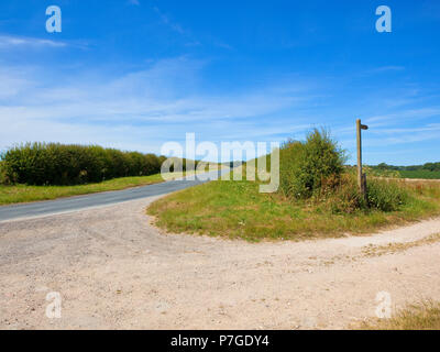 Einer Hochebene aus Kalkstein Reitweg in der Nähe einer Landstraße mit einem hölzernen Wegweiser in der Nähe von Warter mit Blick auf eine kartoffelernte und Wald unter einem blauen Himmel im Yo Stockfoto