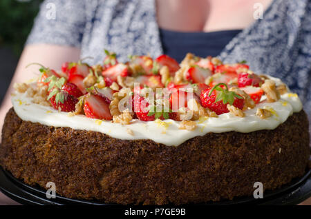 Eine carrotcake mit frischen Erdbeeren und Walnüsse auf einem Auftauen von Frischkäse eingerichtet, Puderzucker und Zitrone. Stockfoto