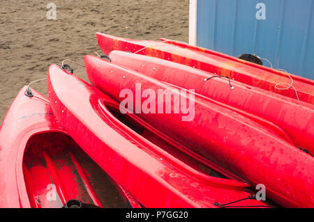 Leeres rotes Plastik Freizeit Kajaks zu mieten oder mieten, am Sandstrand an einem regnerischen Tag gespeichert. Crescent Beach, Surrey, British Columbia, Kanada. Stockfoto