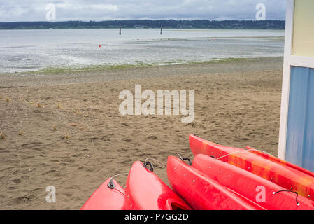 Leeres rotes Plastik Freizeit Kajaks zu mieten oder mieten, am Sandstrand an einem regnerischen Tag gespeichert. Crescent Beach, Surrey, British Columbia, Kanada. Stockfoto