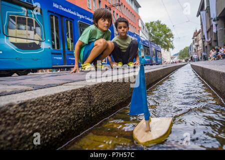 Niños jugando con un barquito de Madera en los Canales de Agua, Münsterplattz, Friburgo de Brisgovia, in Deutschland, in Europa. Stockfoto