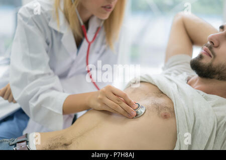 Schöne Frau Doktor in Weiß medizinische Fell untersucht einen Patienten mit einem Stethoskop im Krankenhaus. Ärzte und medizinisches Konzept. Stockfoto