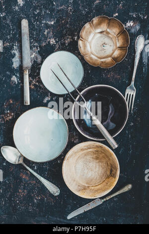 Flach mit Geschirr und Besteck aus verschiedenen Materialien auf einer rostigen dunklen Hintergrund. Foodstyling Konzept Stockfoto