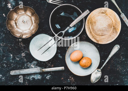 Flach mit Geschirr und Besteck aus verschiedenen Materialien auf einer rostigen dunklen Hintergrund. Foodstyling Konzept Stockfoto