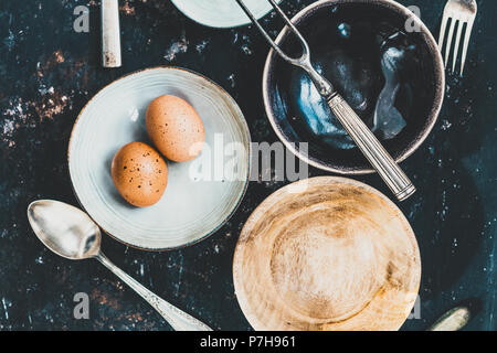 Flach mit Geschirr und Besteck aus verschiedenen Materialien auf einer rostigen dunklen Hintergrund. Foodstyling Konzept Stockfoto