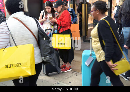 Käufer und Touristen die Einkaufstaschen zu Fuß vorbei am Kaufhaus Selfridges in der Oxford Street in Central London. Stockfoto