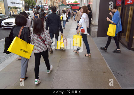 Käufer und Touristen die Einkaufstaschen zu Fuß vorbei am Kaufhaus Selfridges in der Oxford Street in Central London. Stockfoto