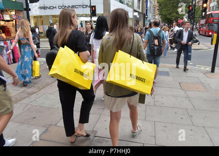 Käufer und Touristen die Einkaufstaschen zu Fuß vorbei am Kaufhaus Selfridges in der Oxford Street in Central London. Stockfoto