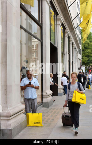 Käufer und Touristen die Einkaufstaschen zu Fuß vorbei am Kaufhaus Selfridges in der Oxford Street in Central London. Stockfoto