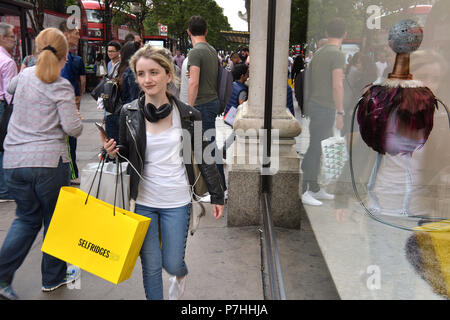 Käufer und Touristen die Einkaufstaschen zu Fuß vorbei am Kaufhaus Selfridges in der Oxford Street in Central London. Stockfoto