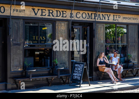 Zwei junge Frauen außerhalb Verde & Unternehmen Cafe, Spitalfields, London, England Sitzen Stockfoto