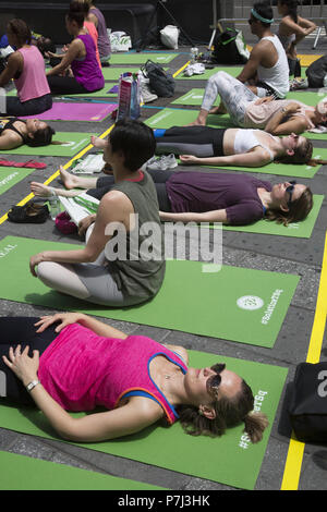 Yoga Enthusiasten nehmen kostenlose Kurse in den jährlichen Times Square Sommersonnenwende Feier mit Klassen den ganzen Tag inmitten der Material glitz der Nachbarschaft, New York City. Stockfoto