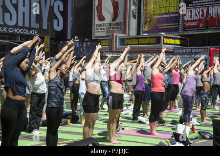 Yoga Enthusiasten nehmen kostenlose Kurse in den jährlichen Times Square Sommersonnenwende Feier mit Klassen den ganzen Tag inmitten der Material glitz der Nachbarschaft, New York City. Stockfoto