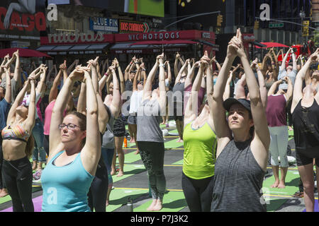 Yoga Enthusiasten nehmen kostenlose Kurse in den jährlichen Times Square Sommersonnenwende Feier mit Klassen den ganzen Tag inmitten der Material glitz der Nachbarschaft, New York City. Stockfoto