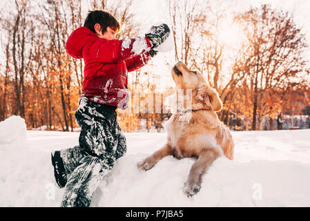 Junge spielt im Schnee mit seinem Golden Retriever Hund Stockfoto