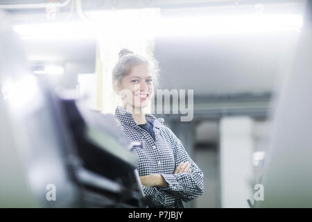 Lächelnde Frau, die in einer Fabrik mit ihren Armen gefaltet Stockfoto