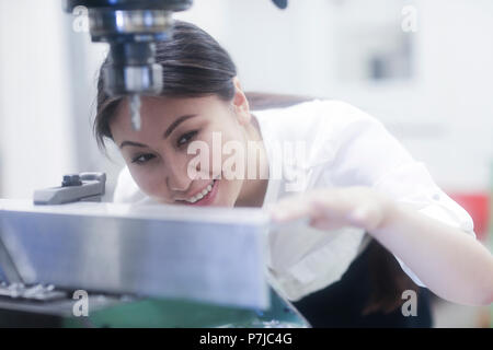 Lächelnd weibliche Ingenieur Vorbereitung ein Loch in einer Metallschiene zu bohren Stockfoto