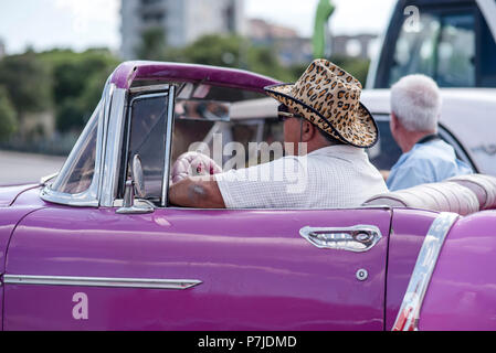 Ein Mann in einem flashy Geparden - Drucken Cowboyhut wartet im Verkehr in seinem violetten Cabrio in Havanna, Kuba. Stockfoto