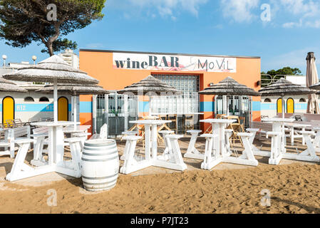 Blick auf die weißen Tischen und Sonnenschirmen vor MoVil Wein Bar, Architektur, die auf den Strand von Lignano Stockfoto