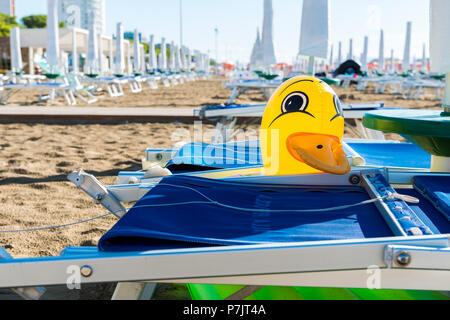 Aufblasbare Ente zwischen blauen Liegestühlen im Sand am Strand von Lignano Stockfoto