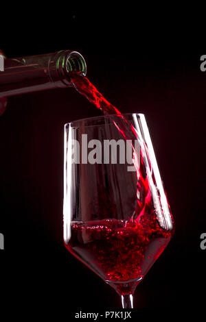 Rotwein gießen Weinglas aus der Flasche auf schwarzem Hintergrund. Weinkarte Menü Design mit Copyspace. Alkohol Getränke Karte Kulisse. Stockfoto