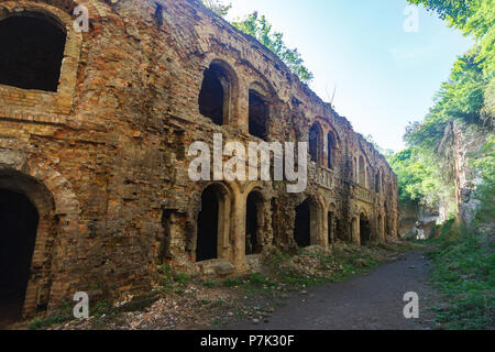 Alte zerstörte Gebäude mit Arkaden bewachsen mit Pflanzen in der Nähe der Wand an einem sonnigen Tag Stockfoto