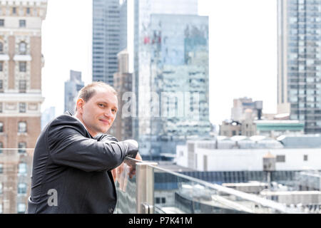 Junge Unternehmer portrait in Anzug, Krawatte, mit Blick auf New York City Skyline Skyline von Manhattan am Wolkenkratzer auf dem Dach glücklich lächelnde Stockfoto