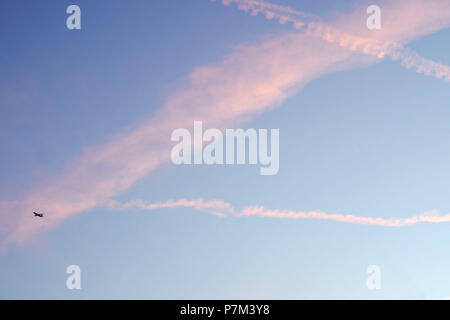 Ein entfernter Passagierflugzeug in den Abendhimmel mit rosa Wolken und Kondensstreifen. Stockfoto