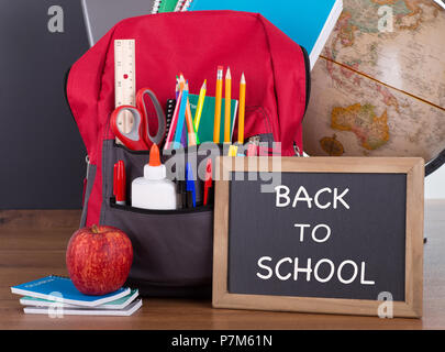 Zurück zu Schule Text auf einer Schiefertafel mit Schulmaterial in einem Rucksack auf einer hölzernen Desktop Stockfoto