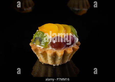 Kuchen Korb mit Kiwi pfirsich Stachelbeeren close-up auf schwarzem Hintergrund Stockfoto