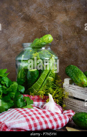 Pickles. Leckere Salzgurken in einem Glas, frische Ernte in einer Holzkiste, Gewürze, Kräuter auf einem Tisch. Vorbereitung von Gurken für Pickles. Vertikale Stockfoto