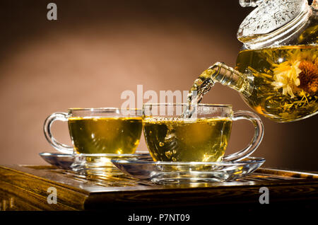 horizontale Foto Glas Teekanne Fluss grüner Tee in Tasse auf braunem Hintergrund, Tee-Zeremonie Stockfoto