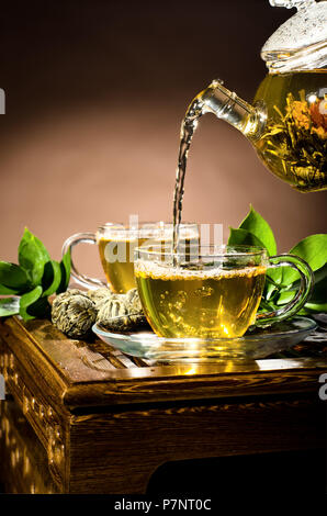 vertikale Foto Glas Teekanne Fluss grüner Tee in Tasse auf braunem Hintergrund, Tee-Zeremonie Stockfoto