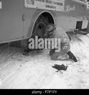 Mann mit der Instandsetzung des Reifens von einem Bus um 1950 im Winter, in der Nähe von Freiburg, Deutschland Stockfoto