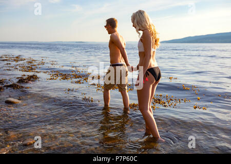 Paar Hände halten und Spaziergänge am Meer am Abend Stockfoto