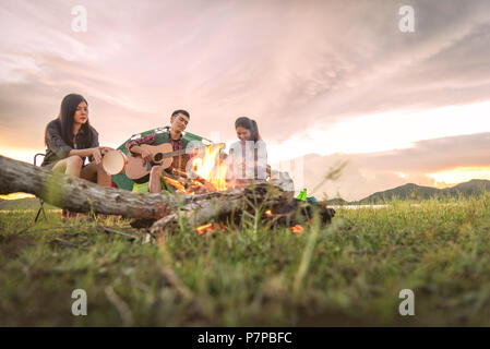 Gruppe von Reisenden, Camping, Picknick und spielen Musik zusammen. Die Berge und den See im Hintergrund. People und Lifestyle. Aktivität im Freien und leis Stockfoto